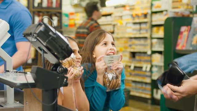 Two little girls run up to their dad in the check out line