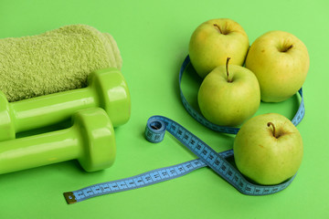Dumbbells in bright green color, rolled measure tape, towel, fruit