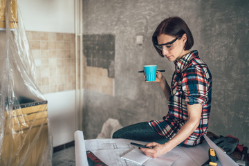 Women using phone and drinking coffee while renovating kitchen