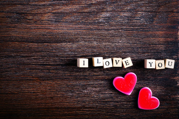 Heart shaped chewing candies and words I love you on cubes, wooden background. Free space for your text.