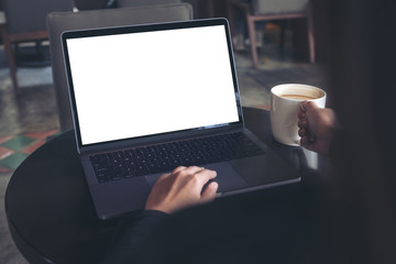 Fototapeta premium Mockup image of business woman using and typing on laptop with blank white screen while drinking coffee in cafe
