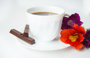  white cup with coffee on white background with flowers of wild orchid and two chocolates