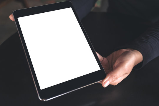 Mockup image of hands holding and showing black tablet pc with white blank screen on table