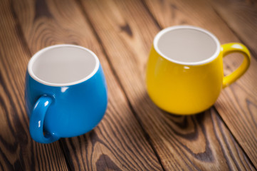 Two colored empty ceramic clean mugs on old worn brown wooden table
