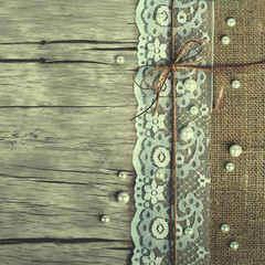 Lace, pearls, bowknot, canvas, sackcloth on wooden background. Toned.