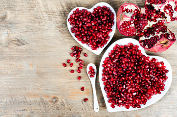 Pomegranate seeds in a shape of a heart on wooden background.