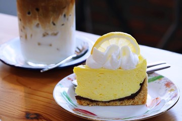 A Lemon meringue pie topped with a large fresh slice lemon placed in white plate and on wooden table with cafe environment. Piece of delicious lemon cake.