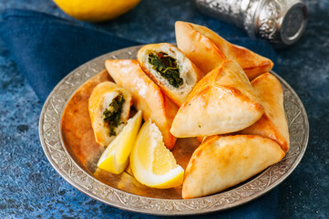 Fatayer sabanekh - traditional arabic spinach triangle hand pies in a vintage plate on a blue stone background.  Close up.