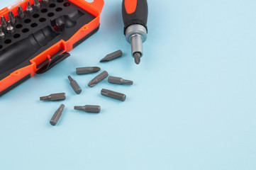 One screwdriver with handle of black and orange color near scattered metal bits and plastic box for bits on blue background with copy space