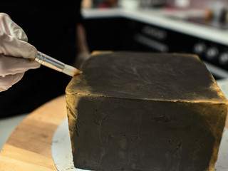 Step-by-step preparation of black designer cake. The confectioner decorates a black cake, gold food paint.