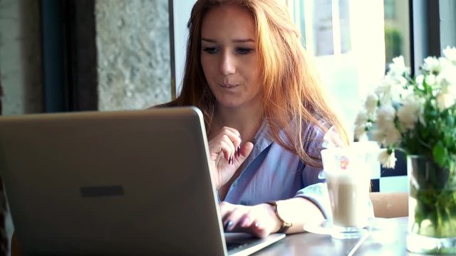 Young, pretty woman with red hair using laptop in cafe
