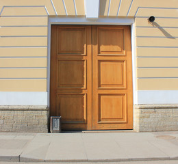Wooden Door on Old Historic Building Facade. Street View with Simple Cloosed Wood Door Frame on Classical House of Soft Yellow Colored Exterior Wall. City Scene with Retro Doorframe Entrance.