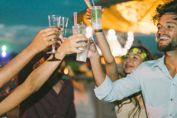 Group of happy friends cheering with cocktails at beach after sunset party