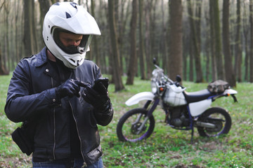 Fototapeta na wymiar classic enduro motorcycle off road in spring forest, man in a stylish leather jacket uses a smartphone, Motorcyclist gear, A motorcycle driver looks, concept, active lifestyle