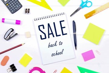 A blank notebook page surrounded by stationery on a white wooden table. Back to school sale.