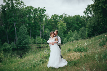 Happy stylish bride and groom walking on the river, smiling and kissing