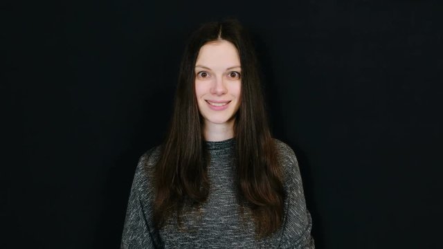 Young attractive brunette woman winks one eye while looking at the camera in black background. Room for text.