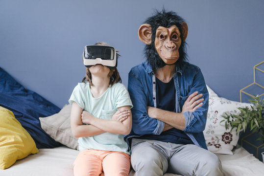 Father wearing monkey mask sitting next to son wearing VR glasses at home