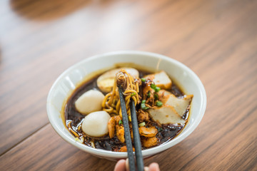 Soft focus hand with Chinese chopsticks eating noodle, a famous Malaysia Loh Mee.