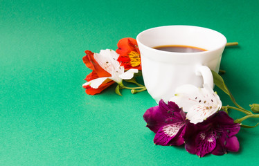 White cup with coffee in orchid flowers on a green background