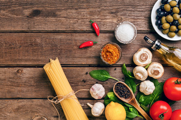 Pasta ingredients - tomatoes, olive oil, garlic, italian herbs, fresh basil, salt and spaghetti on a wooden background with copy space, horizontal, top view