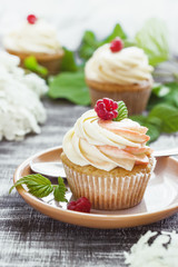 Delicate vanilla cupcakes with cream and raspberries on a dark wooden background