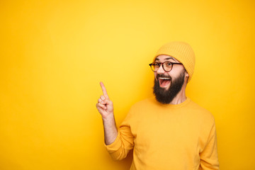 Excited hipster pointing up on yellow