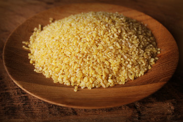 Dry bulgur wheat in wooden bowl isolated Spilled bulgur