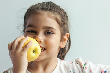 A cute little girl eating fresh vegetables. A portrait on white background. Healthy teeth.