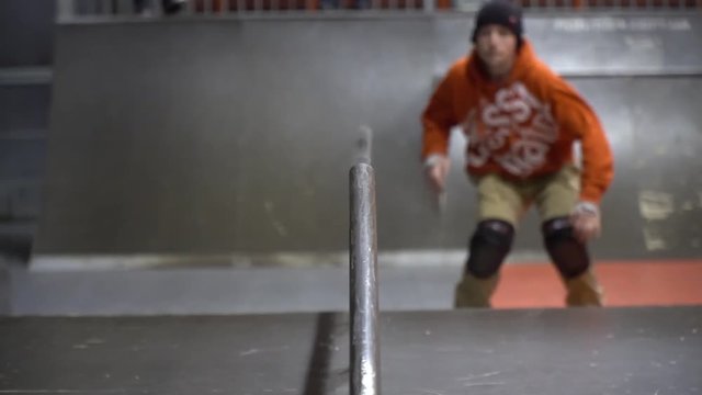 A man in an orange sweatshirt skates in a skate park on rollers, slow motion