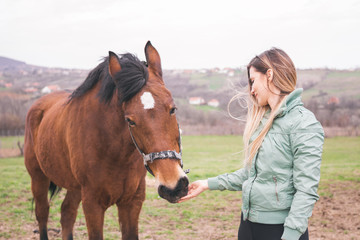 Fototapeta premium Beautiful young woman on the ranch bonding with a brown horse. 