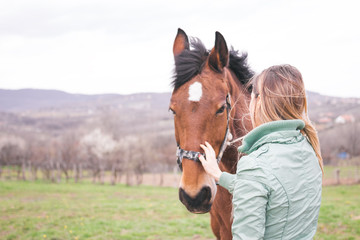 Fototapeta premium Beautiful young woman on the ranch bonding with a brown horse. 