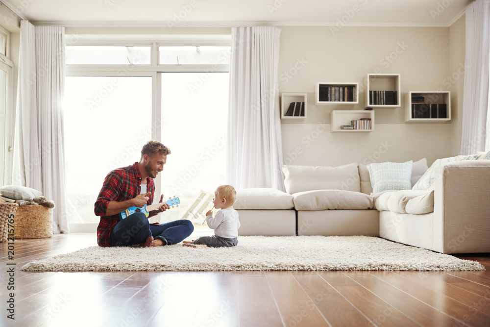 Wall mural Father playing ukulele with young son in their sitting room