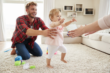 Toddler girl walking from dad to mumÕs arms in sitting room