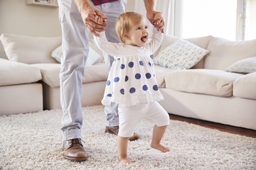 Father helping daughter learn to walk in the sitting room