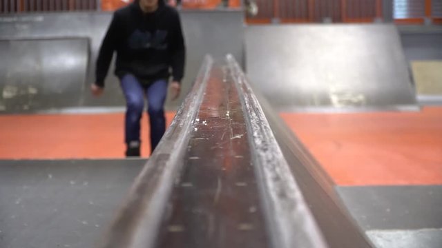 Front view as a man on rollers performs a grind on the railing in the skate park, slow motion. Niffty