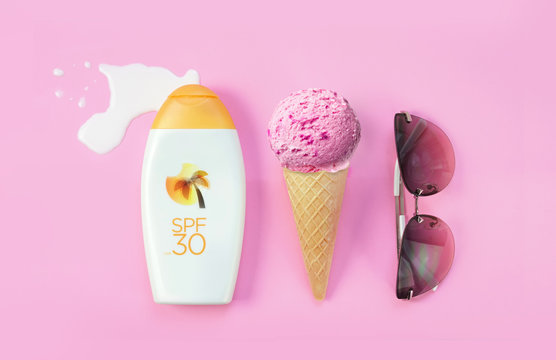 Creative layout concept for summer holidays. A set of sunglasses, ice cream cone and bottles of lotion against sunburn on a pink background.