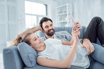 Lovely photos. Cheerful young happy couple smiling and taking lovely photos while relaxing on a comfortable sofa