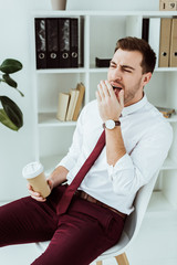 tired businessman with coffee yawning in modern office