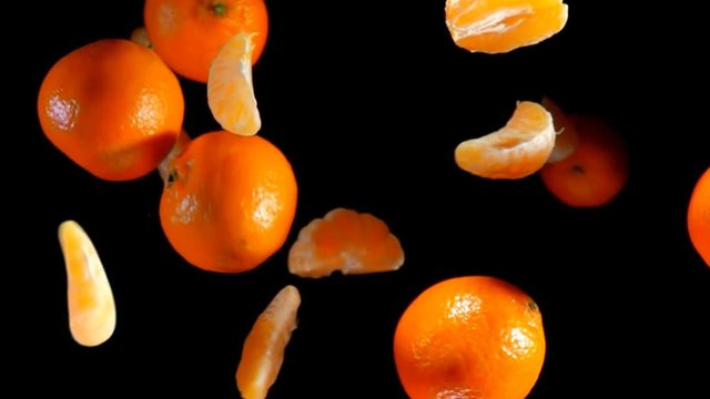 Slices and whole mandarins bouncing against to the camera on a black background in slow motion