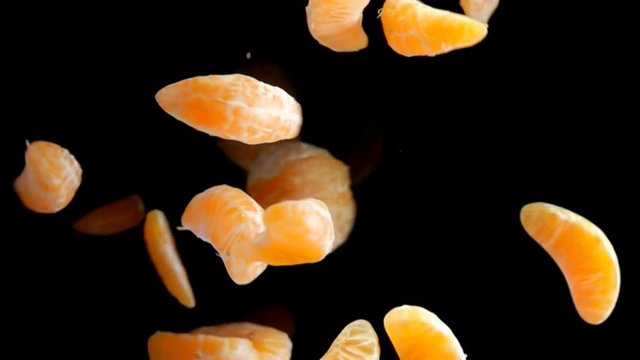 Slices and halves of mandarin flies to the camera on a black background in slow motion