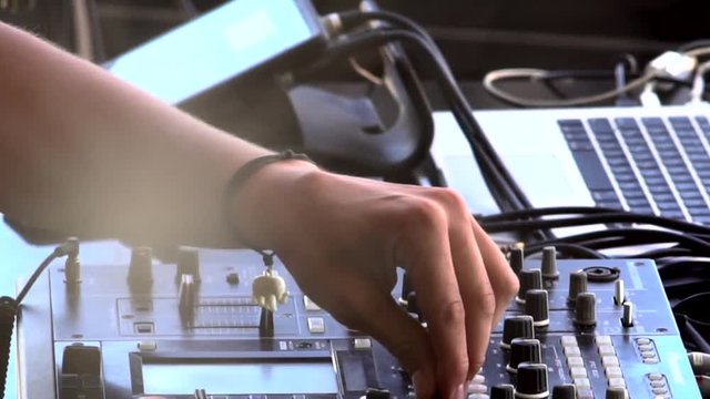 DJ hands touch buttons and sliders on sound mixing controller deck with laptops, monitors and wires, close-up. Disc jockey mix tracks, play electronic music on pro audio equipment in beach club.