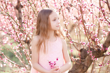Fototapeta na wymiar Baby girl 4-5 year old posing peach flowers outdoors. Looking away. Spring season.