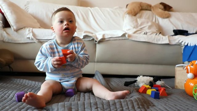 Cute baby boy with Down syndrome playing with toy in home living room