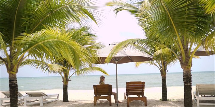  A beautiful girl in a swimsuit lies on a lounger under the malmas. A girl is resting by the sea. The girl is lying on the deckchair. Girl under the palm trees.