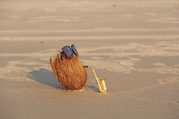 A coconut on the beach wearing sunglasses plays on a gold alto saxophone. Creative, humor and surrealism. Musical cover