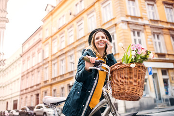 Naklejka premium Young woman with bicycle and smartphone in sunny spring town.