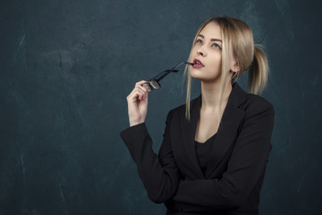 Fototapeta premium Portrait of a beautiful woman in glasses in a black suit against a blue textural wall with space for text.