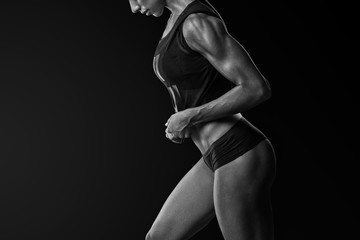 Confident athletic woman bodybuilder with sixpack abs posing Young fitness woman in sports clothing bra short standing with hands overhead Black and white close-up shot.