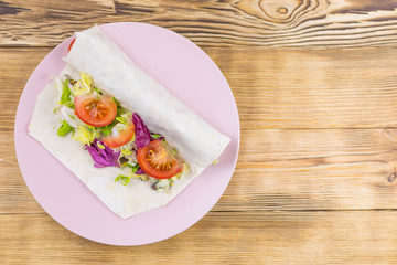 Preparation of a roll of pita bread and fresh vegetables on a wooden background. The concept of healthy eating.